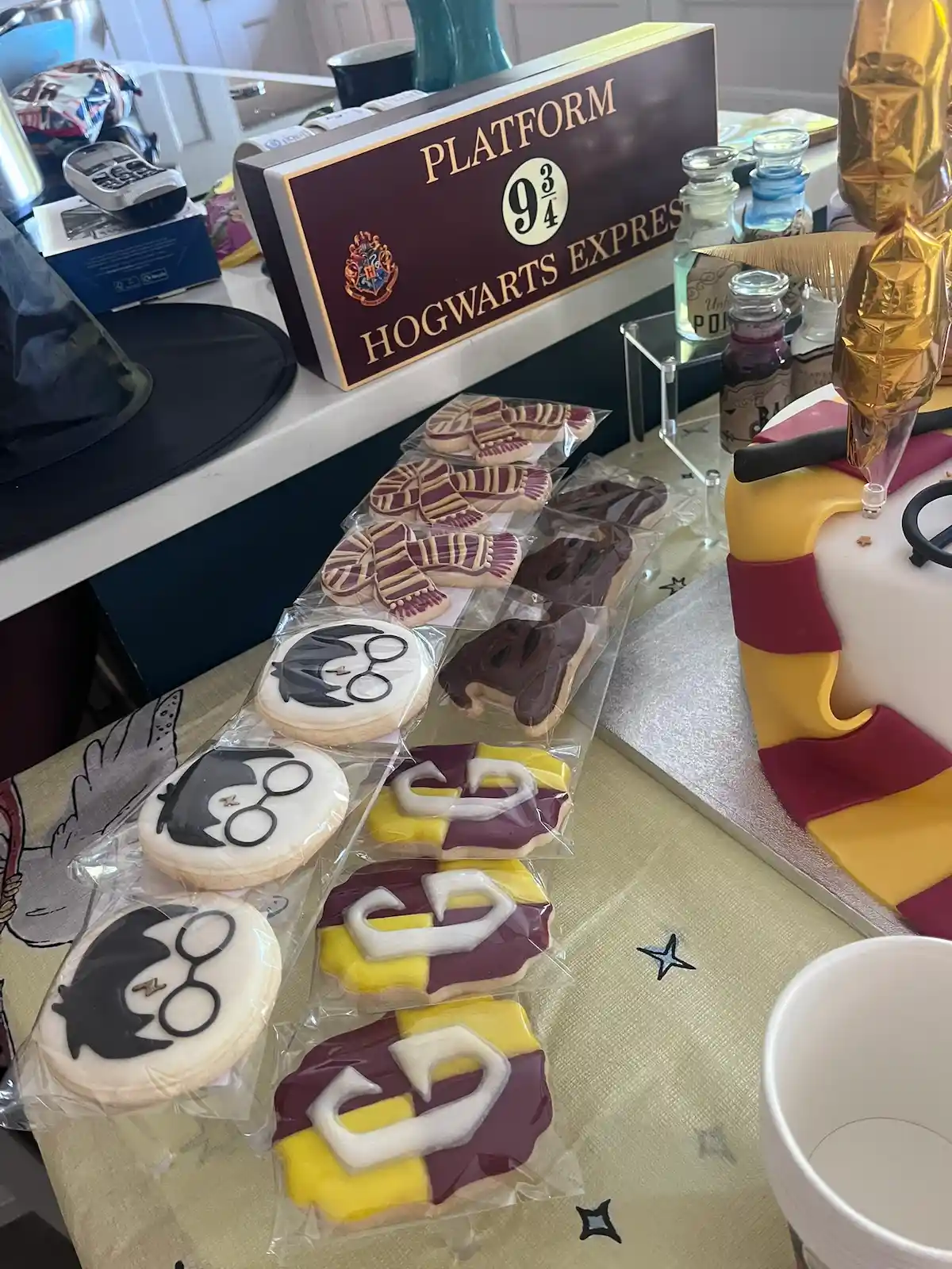 Harry Potter themed cookies decorated with glasses, scarves and wizard-inspired designs displayed beside a Platform 9¾ sign.