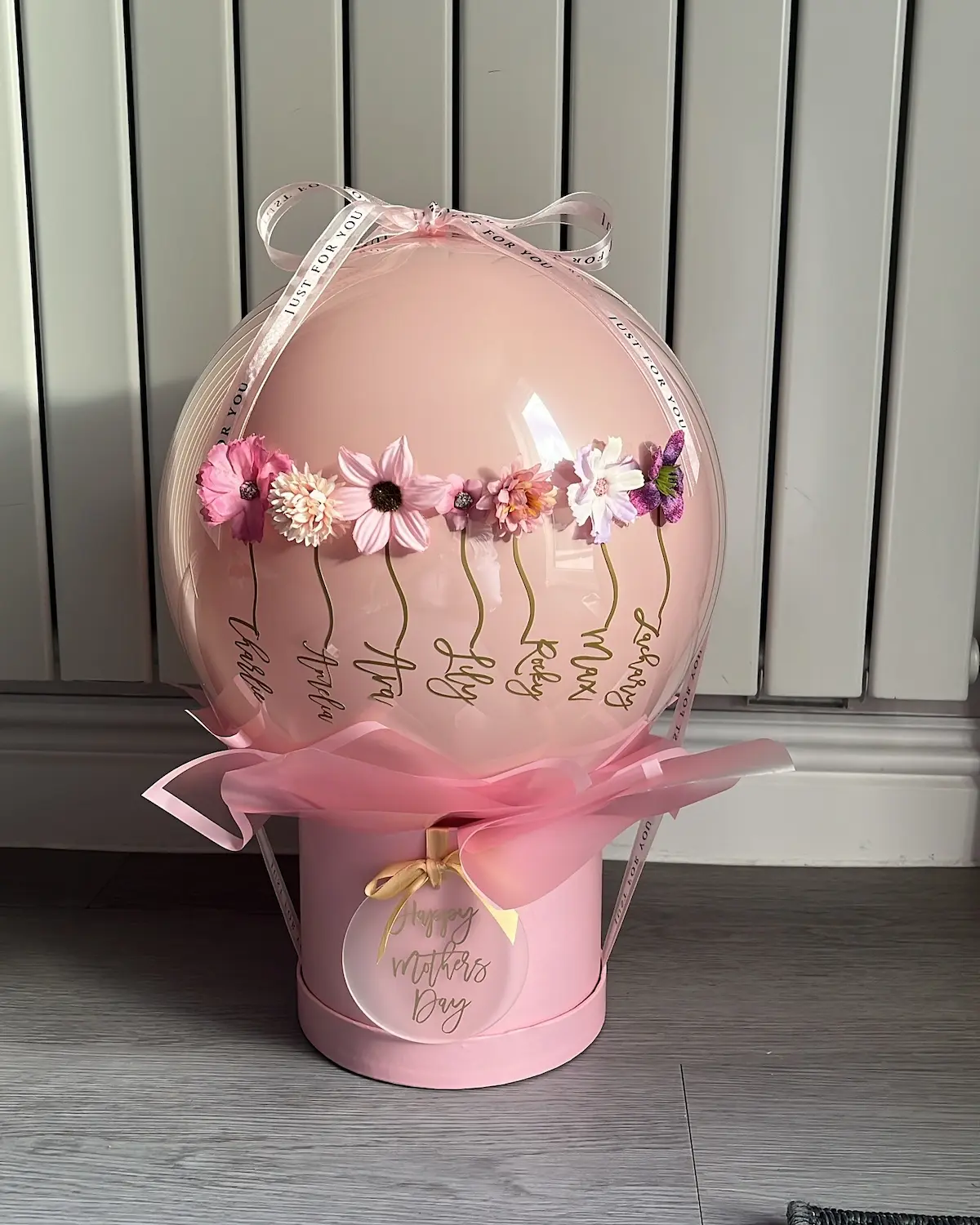 Personalised Mother's Day balloon gift featuring children's names as flower stems , sat on a pink hat box