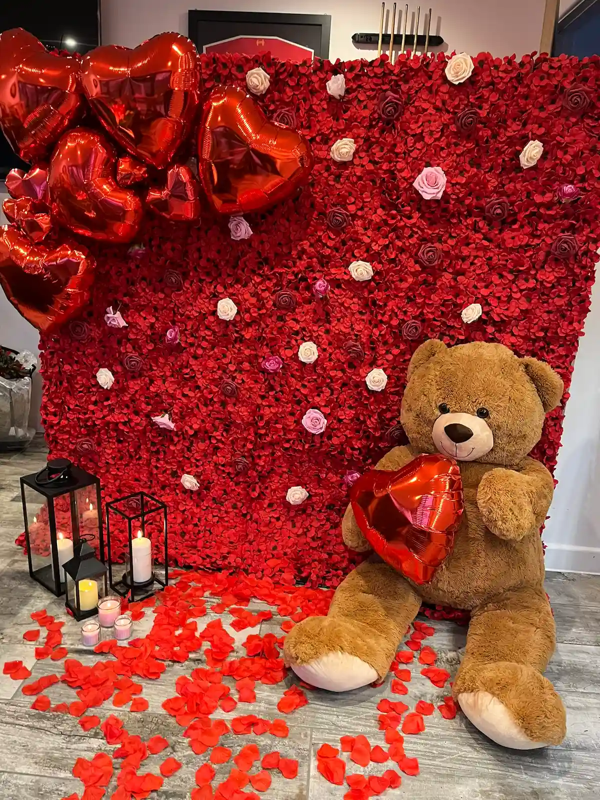 Valentine's Day display with red flower wall backdrop, teddy bear, heart balloon, lantern and rose petals